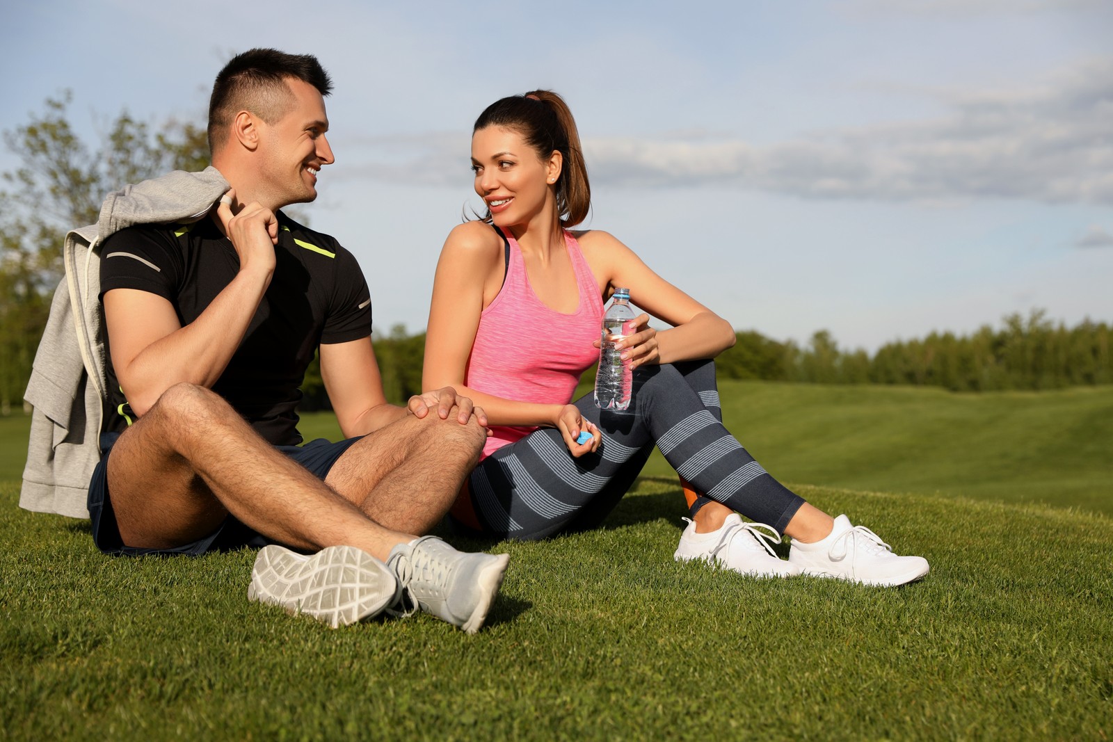 Photo of man and woman in fitness clothes resting on green grass outdoors