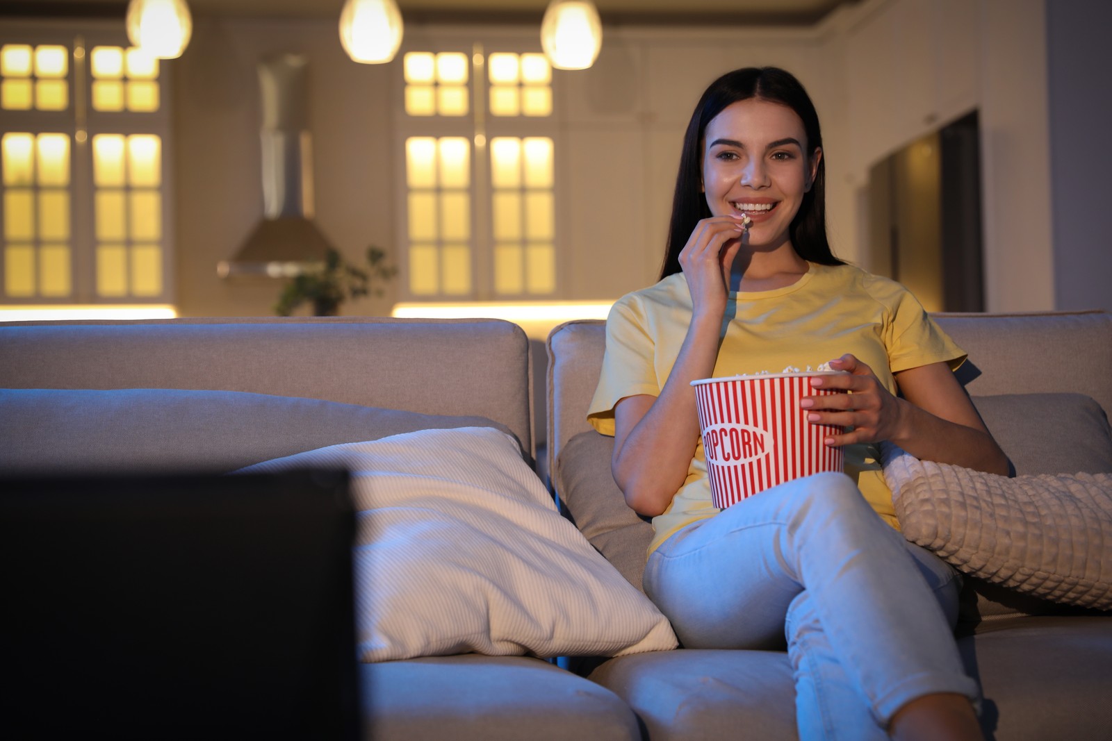 Photo of young woman watching movie with popcorn on sofa at night, space for text