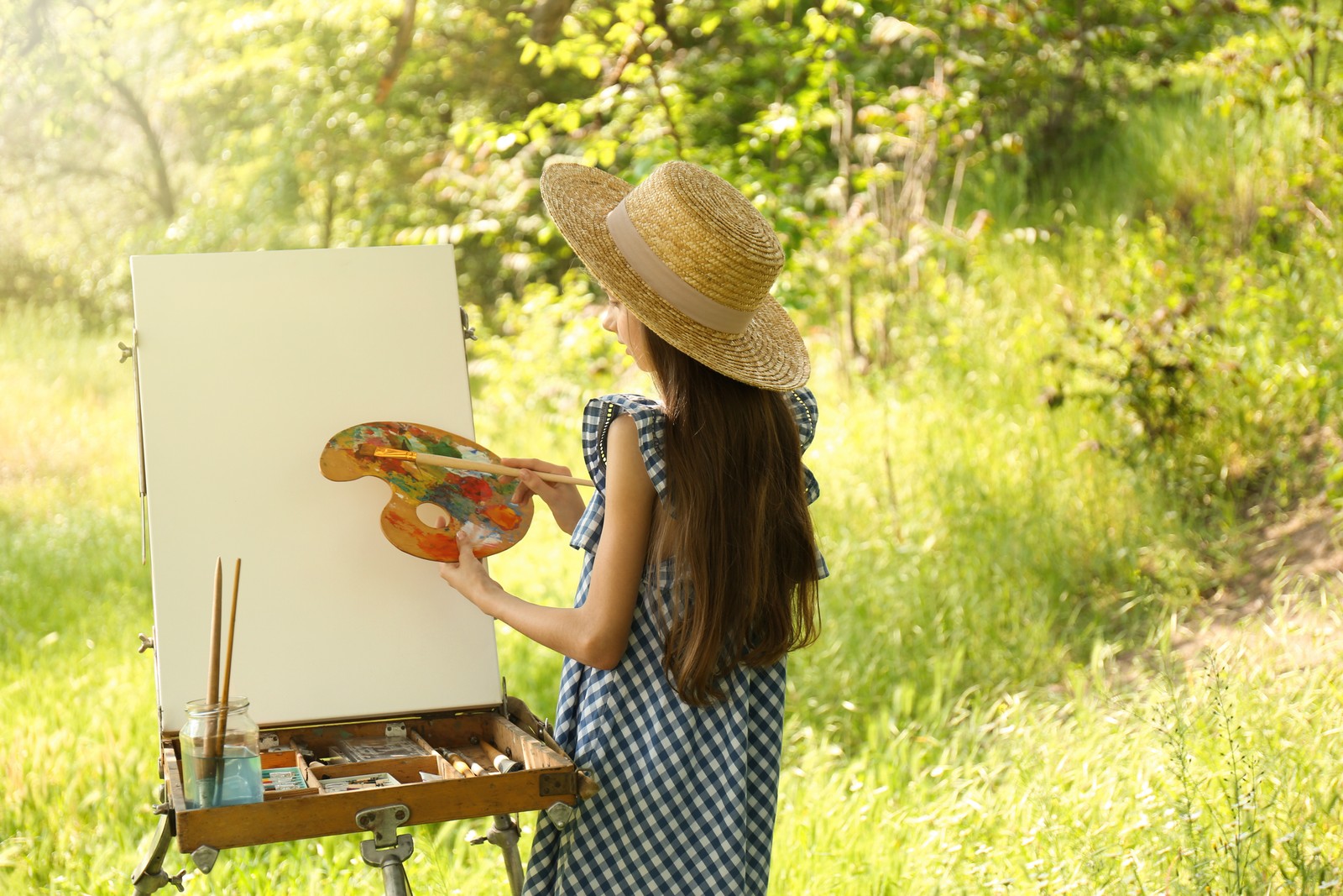 Photo of little girl painting on easel in picturesque countryside