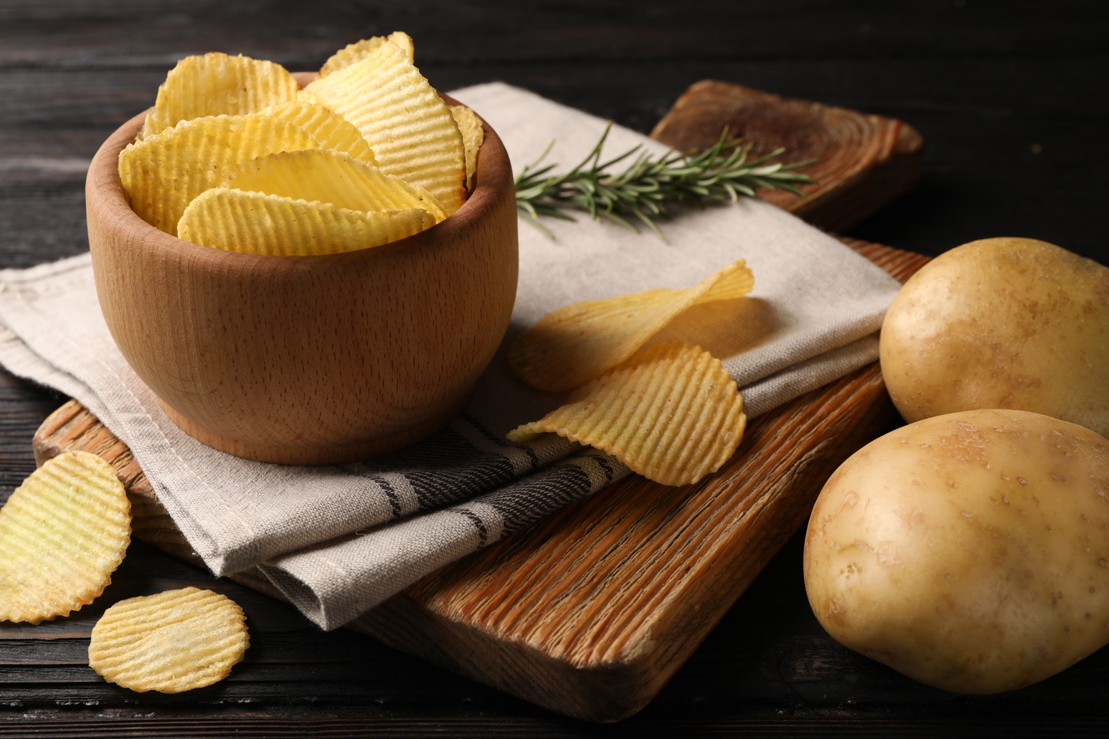 Photo of bowl of crispy potato chips on wooden table