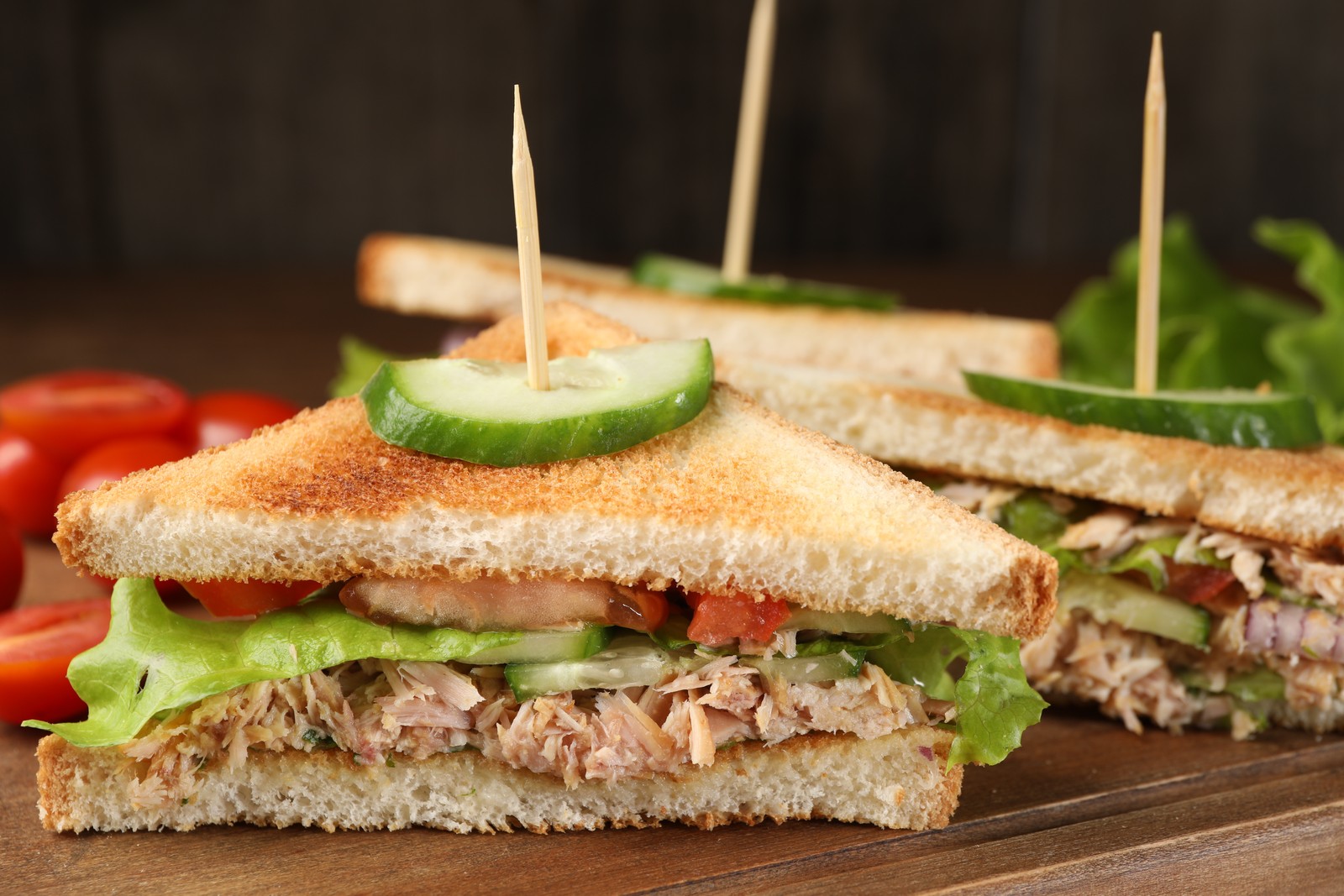 Photo of delicious sandwiches with tuna and vegetables on wooden board, closeup