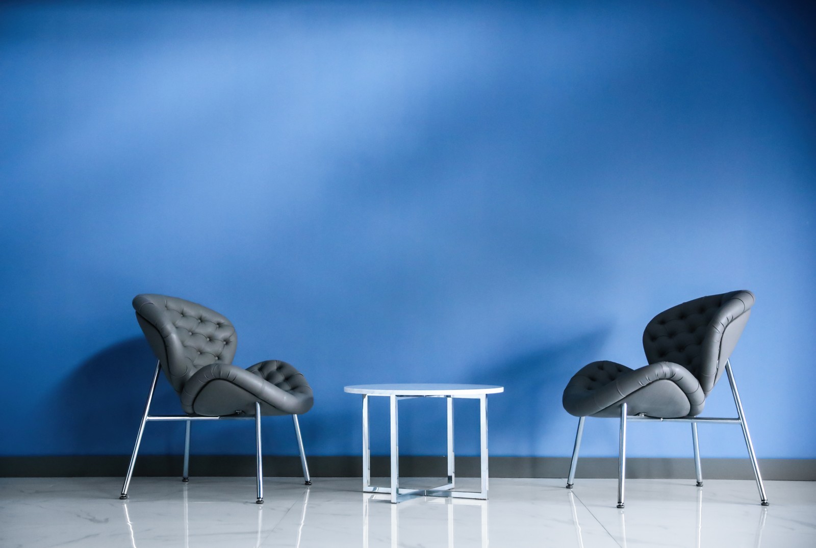 Photo of comfortable armchairs and metal table near blue wall. Modern room interior