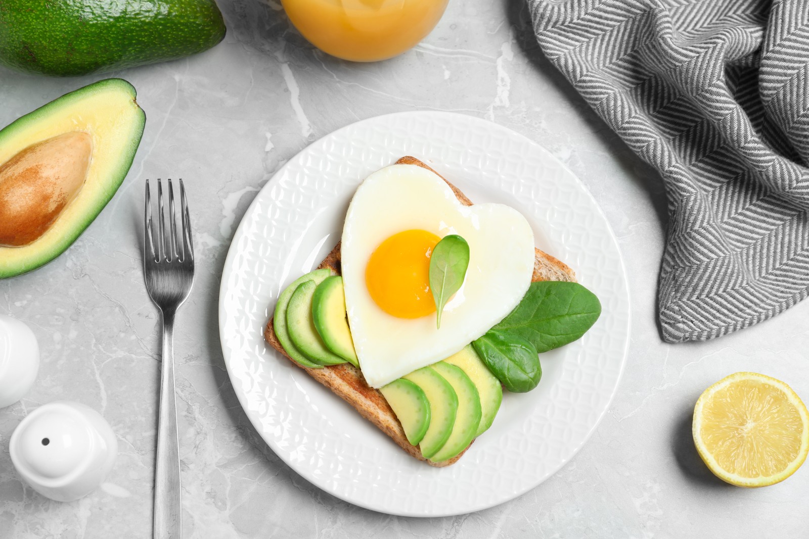 Photo of tasty breakfast with heart shaped fried egg served on grey table, flat lay