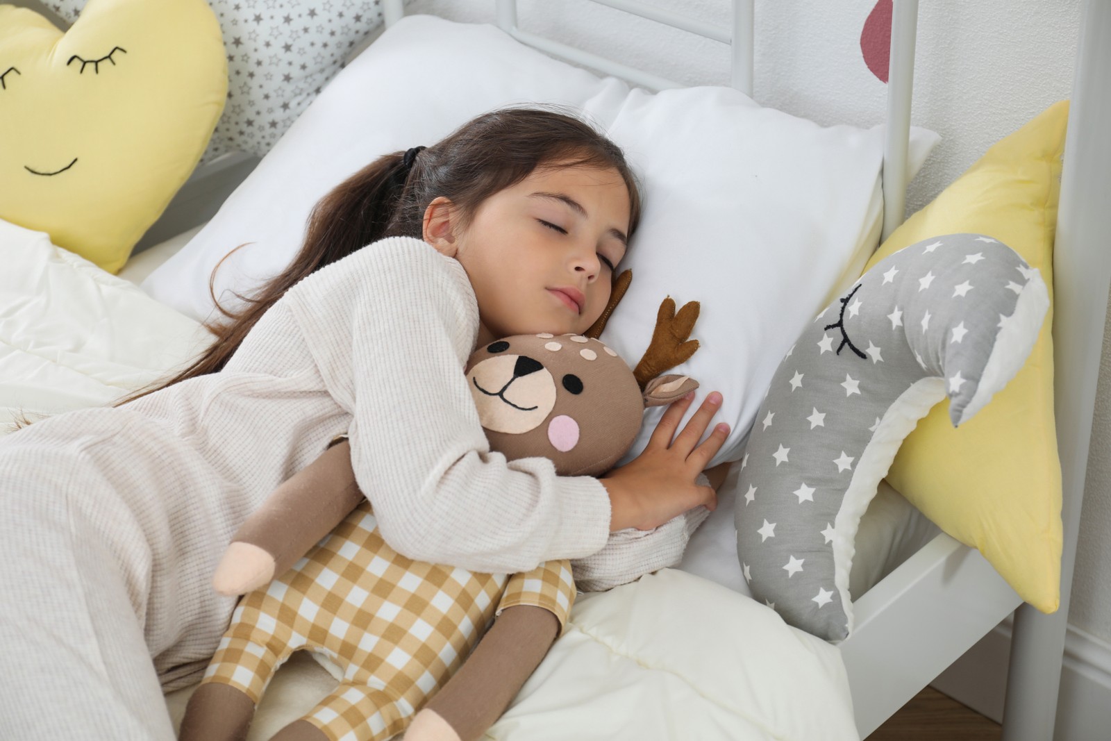 Photo of cute girl in pajamas sleeping with toy deer at home