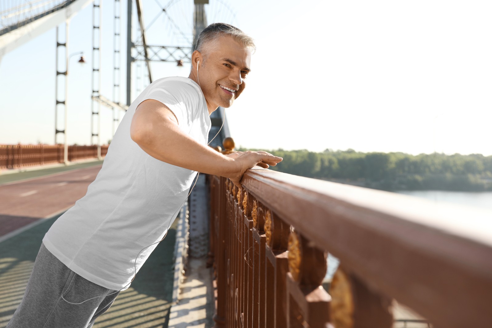 Photo of handsome mature man in sportswear doing exercise on bridge. Healthy lifestyle