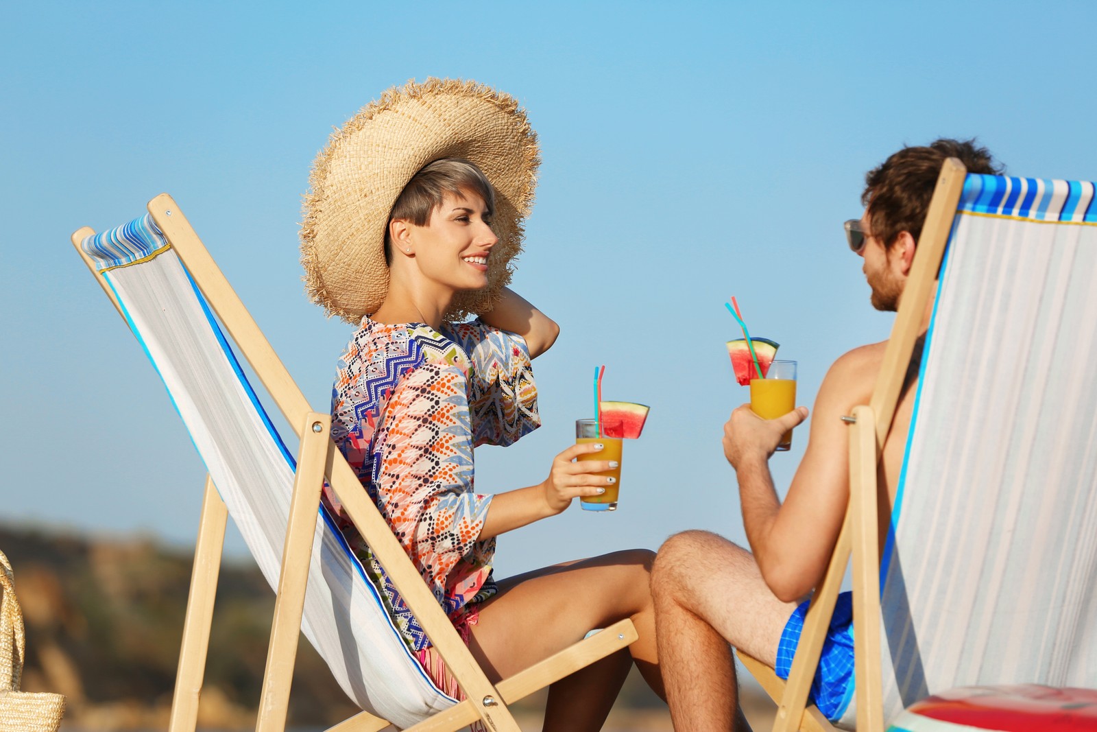 Photo of young couple with cocktails in beach chairs at seacoast