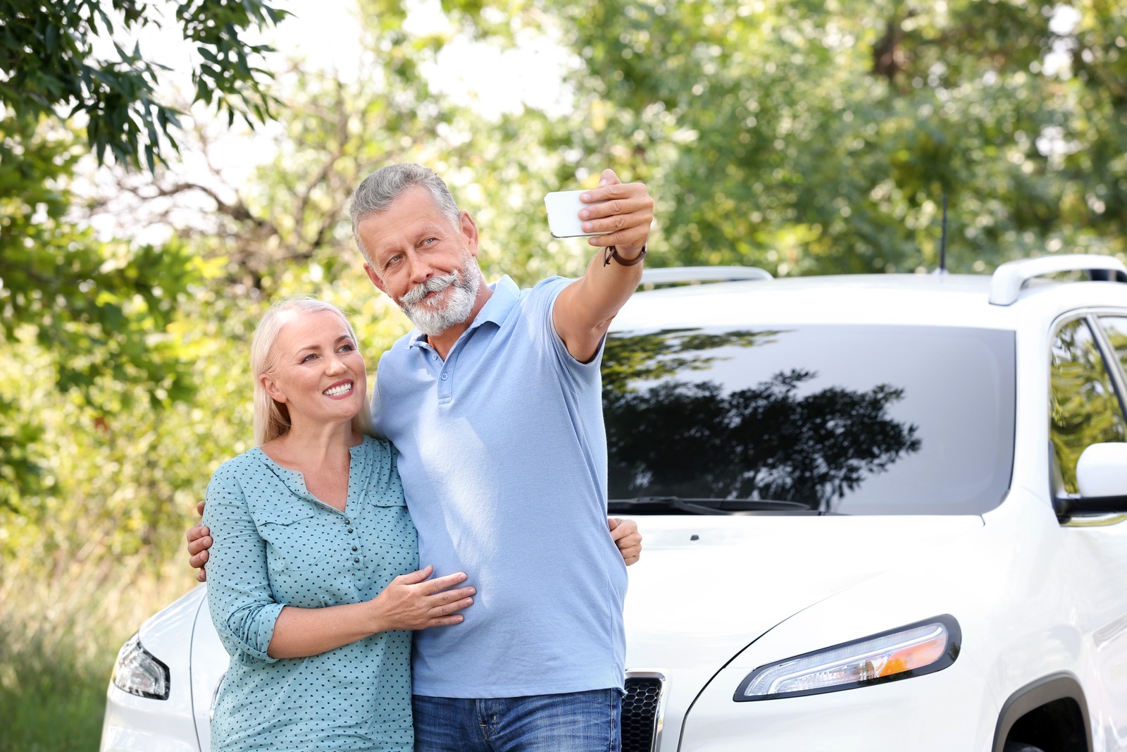 Photo of happy senior couple taking selfie near car outdoors