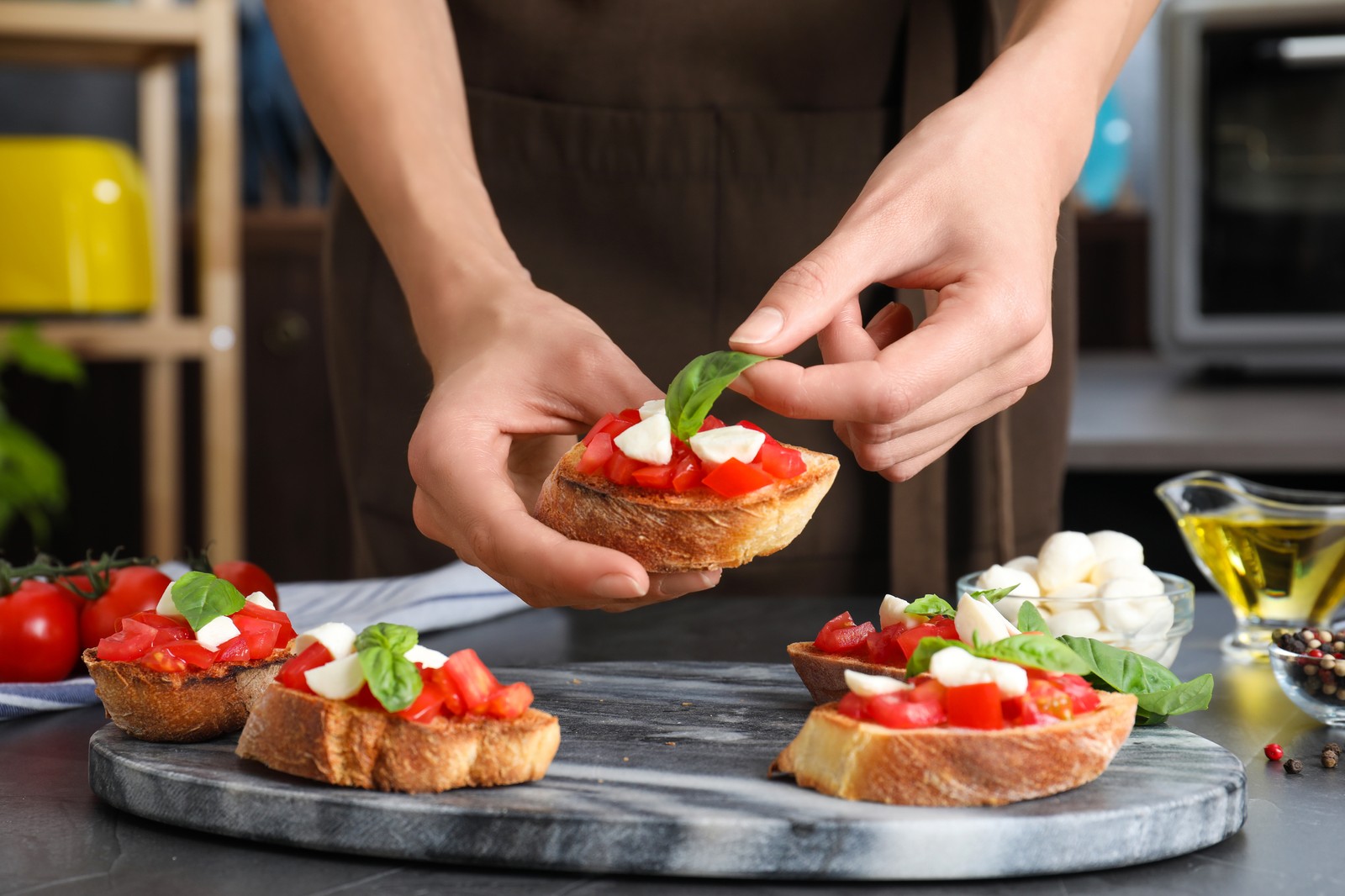 Photo of woman preparing delicious bruschettas with cheese and tomatoes at table, closeup