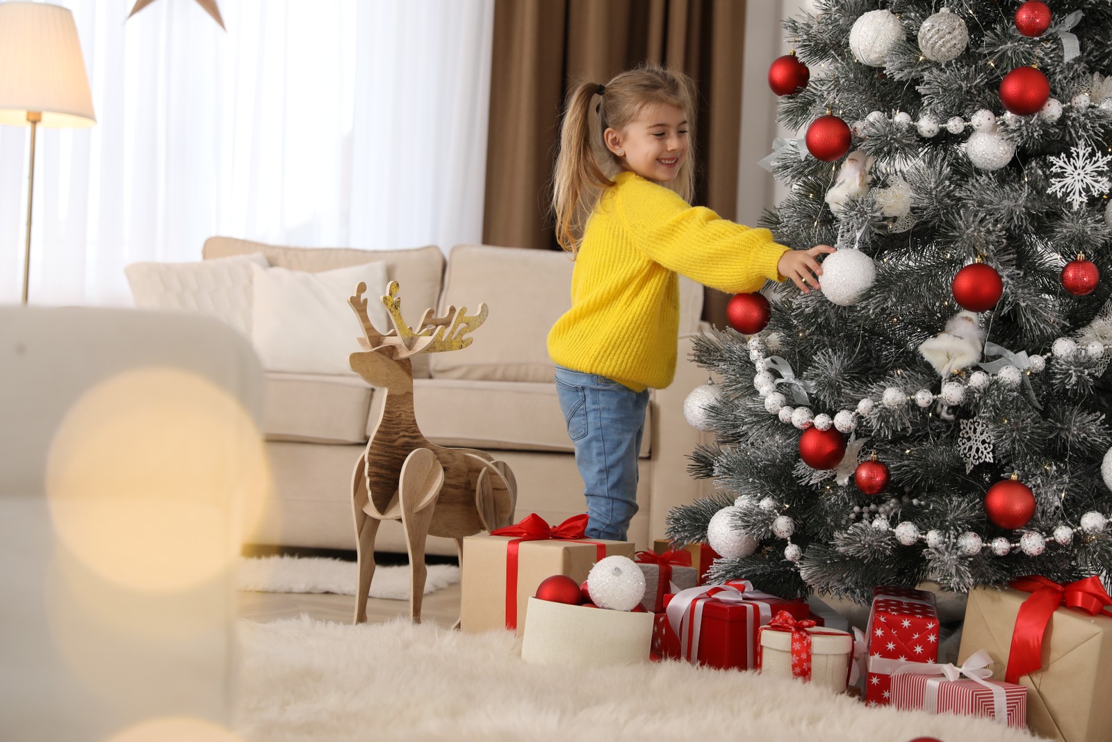 Photo of cute little girl decorating Christmas tree at home
