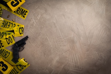 Flat lay with yellow tape, crime scene marker and gun on grey stone background. Space for text