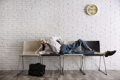 Human skeleton in office wear lying on chairs near brick wall indoors