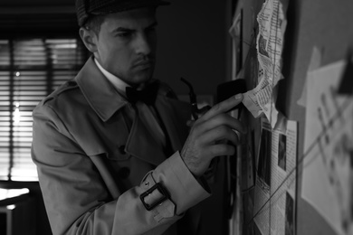 Old fashioned detective with smoking pipe near investigation board in office. Black and white effect