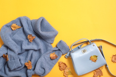 Warm sweater, bag and dry leaves on yellow background, flat lay with space for text. Autumn season