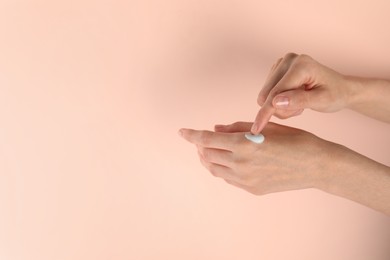 Woman applying hand cream on pink background, closeup. Space for text