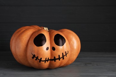 Pumpkin with drawn spooky face on grey table, space for text. Halloween celebration