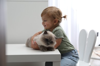 Cute little child with adorable pet at white table in room