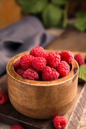 Bowl of fresh ripe raspberries on wooden board, closeup