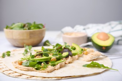 Photo of Tortilla with hummus and vegetables on table, closeup