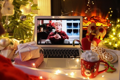MYKOLAIV, UKRAINE - DECEMBER 23, 2020: Woman with sweet drink watching Home Alone movie on laptop at home, closeup. Cozy winter holidays atmosphere