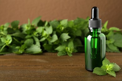 Glass bottle of nettle oil with dropper and leaves on wooden table, space for text