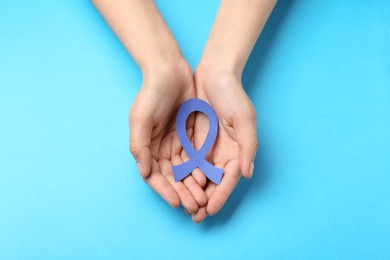 Woman holding blue awareness ribbon on color background, top view. Symbol of social and medical issues