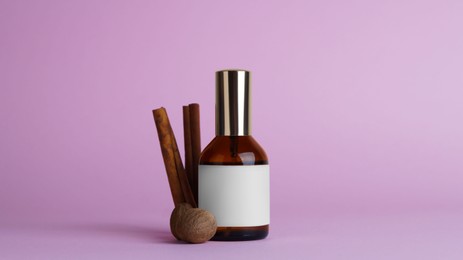 Photo of Bottle of luxurious perfume and spices on light purple background
