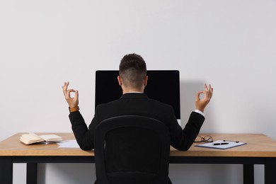Businessman meditating at workplace, back view. Zen concept