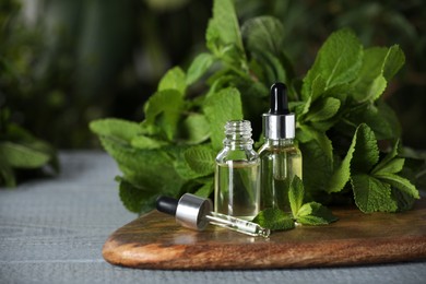 Bottles of mint essential oil, pipette and green leaves on grey wooden table, space for text