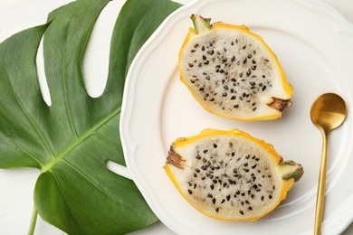 Plate with delicious cut dragon fruit (pitahaya) and tropical leaf on white wooden table, flat lay