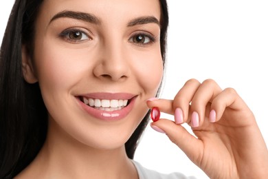 Young woman with vitamin capsule on white background, closeup