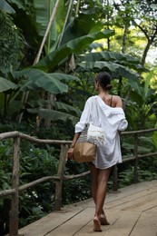 Young woman walking in green tropical park, back view