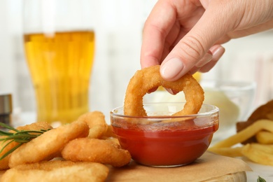 Woman dipping crunchy fried onion ring in tomato sauce, closeup