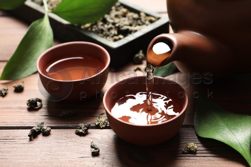 Pouring Tie Guan Yin oolong tea into cup on wooden table