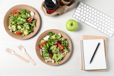 Photo of Plates of fresh salad, keyboard, apple, notebooks and cutlery on white wooden table, flat lay. Business lunch