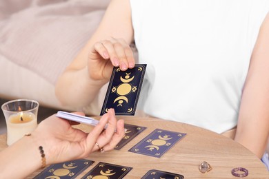 Photo of Woman pulling one tarot card at table indoors, closeup. Fortune telling