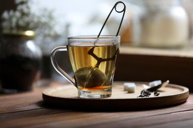 Cup of freshly brewed tea with snap infuser and sugar cubes on wooden table indoors