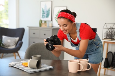 Photo of Young photographer taking picture of cups at table indoors
