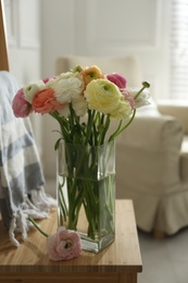 Beautiful ranunculus flowers in vase on wooden chair indoors