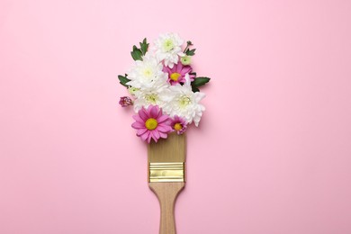 Brush with colorful flowers of chrysanthemum on light pink background, top view. Creative concept