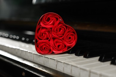 Photo of Beautiful red roses in heart shaped box on piano keys, closeup