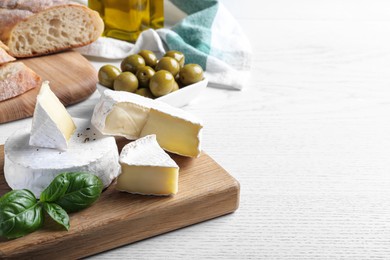Tasty brie cheese with basil on white wooden table, space for text