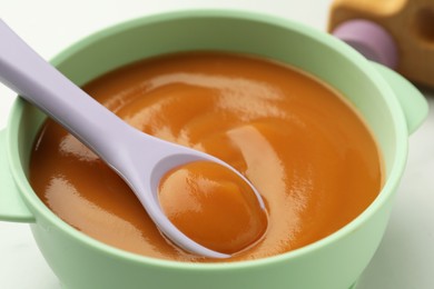 Bowl and spoon with tasty pureed baby food on table, closeup