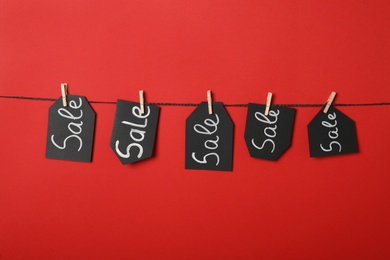 Tags with word Sale hanging on rope against red background. Black Friday concept
