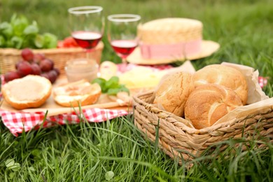 Picnic blanket with wine and snacks outdoors, focus on buns in wicker basket
