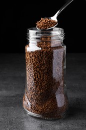 Instant coffee and spoon above glass jar on grey table against black background