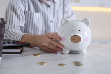 Woman with piggy bank at marble table indoors, closeup