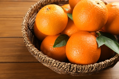 Delicious ripe oranges in wicker bowl on wooden table, closeup