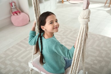 Cute little girl playing on swing at home