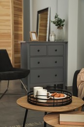 Photo of Tray with cups of hot tea and cookies on wooden table in living room. Interior design