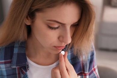 Upset young woman taking abortion pill on blurred background, closeup